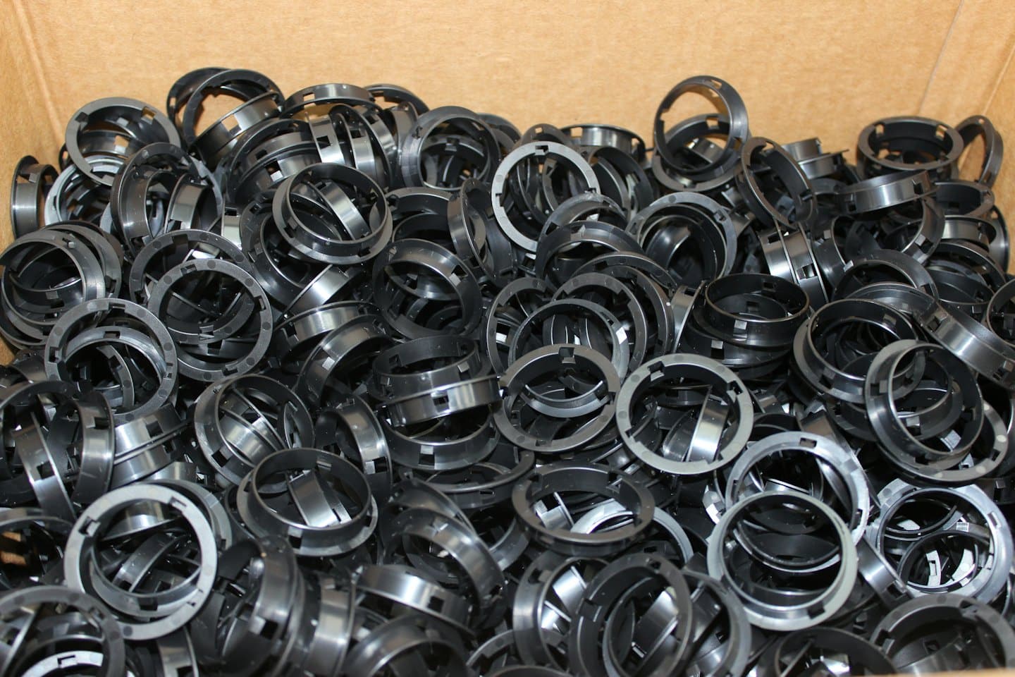 Molti piccoli componenti neri di ruote di plastica accatastati dentro una scatola.