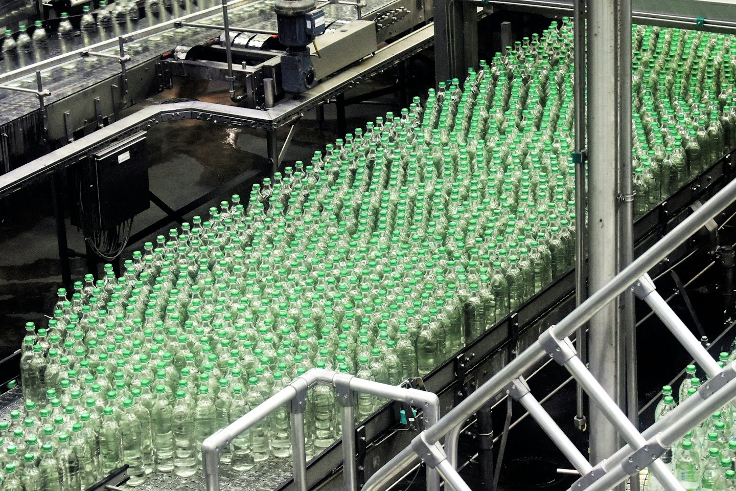 Bottiglie di plastica con tappi verdi su un nastro trasportatore in una fabbrica.